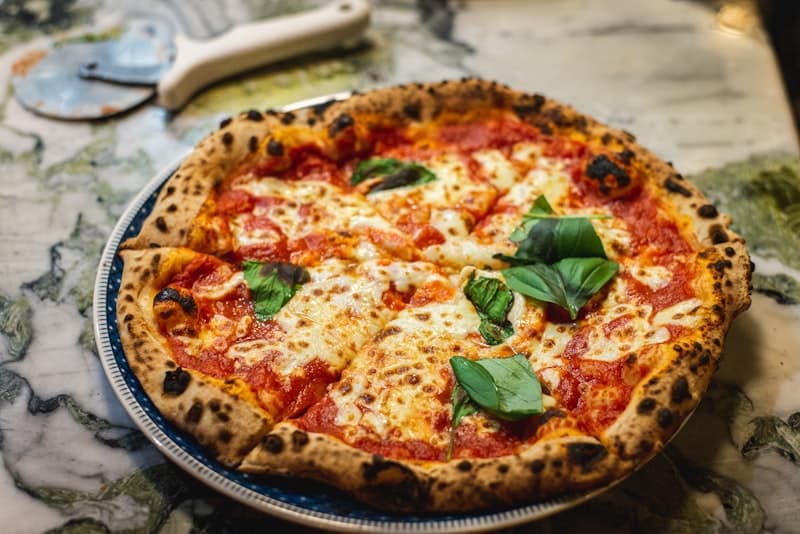 Houtoven pizza met nduja worst, romige burrata en verse rucola op een donker bord